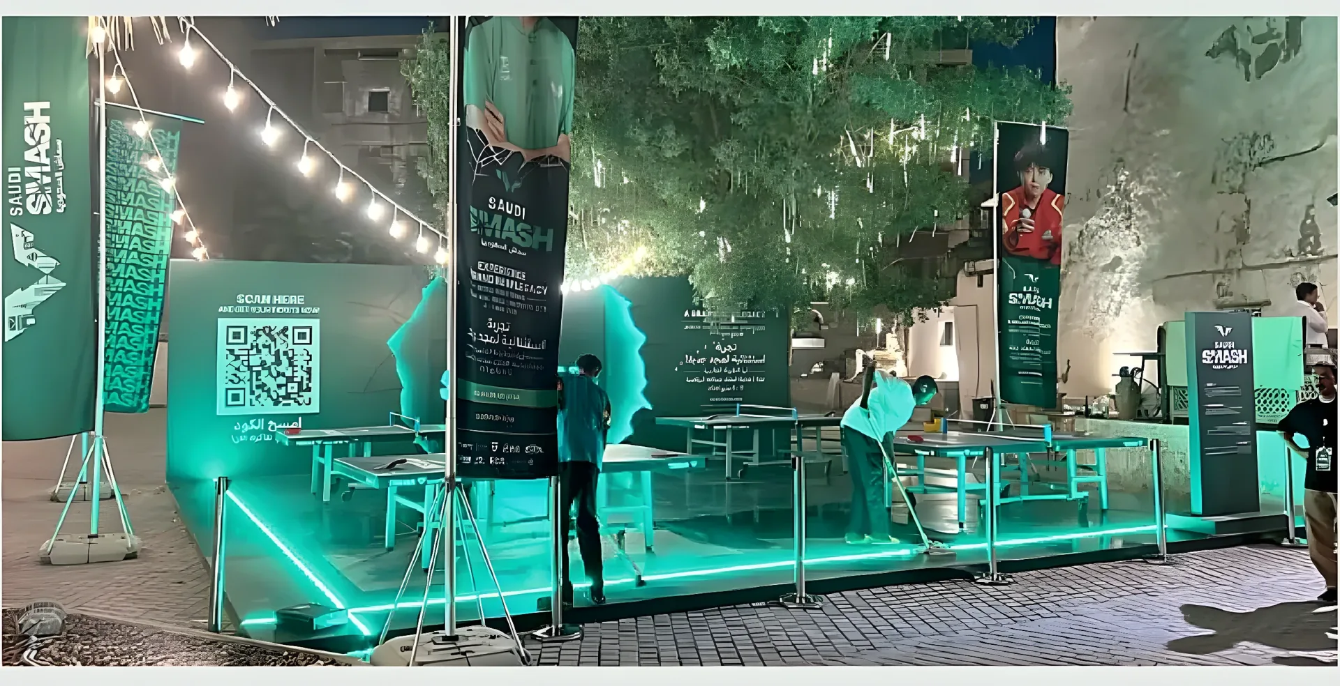 جناح سماش السعودية مضاء بالنيون تحت الأشجار ليلًا